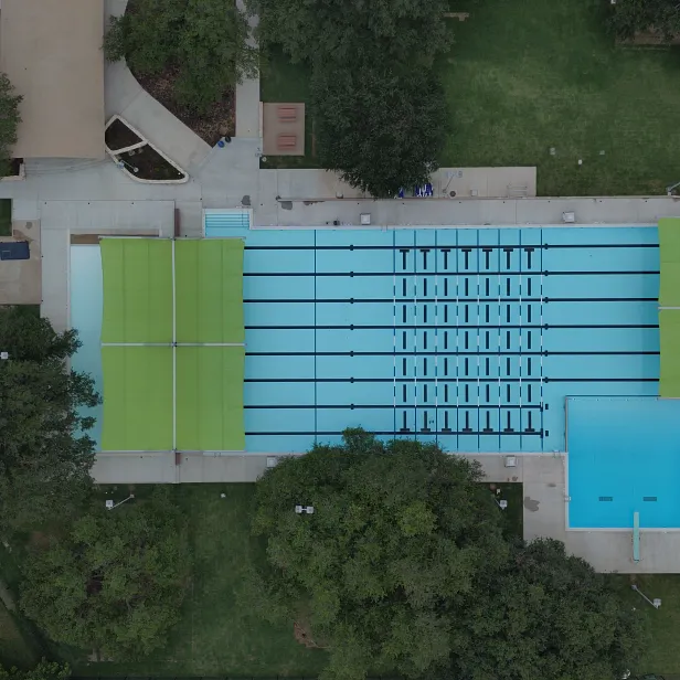 Aerial view of the renovated Sheffield Northwest District Park pool complex, showing the 50-meter lap pool, zero-entry toddler pool, and shade structures surrounded by trees